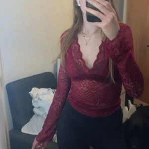 Röd spetsblus med v-ringning - Säljer en röd långärmad blus i spets med v-ringning och transparenta detaljer. Blusen har figurnära passform och fina spetsmönster över hela plagget. 