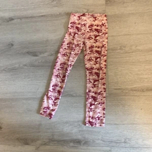 Rosa och röda camo-leggings - Säljer ett par leggings med rosa och rött camouflage-mönster. Byxorna är tighta och har elastiskt material som gör dem bekväma att bära. Perfekta för dig som gillar färgglada och unika plagg. Jätte skönt tyg dom har ett litet hål på knät men inget man tänker på.