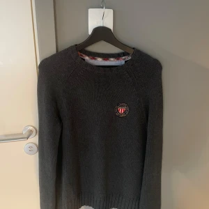 Mörkgrå stickad tröja från Ralph lauren  - Säljer en mörkgrå stickad tröja med rund hals och ett broderat emblem på bröstet. Tröjan har långa ärmar och ribbade muddar vid ärmslut och nederkant. Hör gärna av dig vid frågor🙌