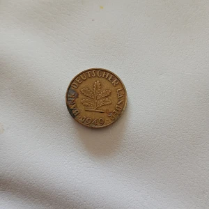 10 Pfennig mynt från 1949 - Säljer ett tyskt 10 Pfennig mynt från 1949. Myntet är i metall och har en ekkvist på ena sidan samt texten 'BANK DEUTSCHER LANDER'. På andra sidan står valören 10 Pfennig med en lagerkrans runt siffran.