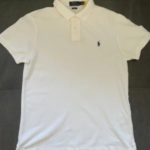 Ralph Lauren pike - Klassisk vit pikétröja från Polo Ralph Lauren med broderad logga på bröstet. Slim fit-modell med korta ärmar.                                                                       Storlek:L.                                                                            Skick: Mycket bra.