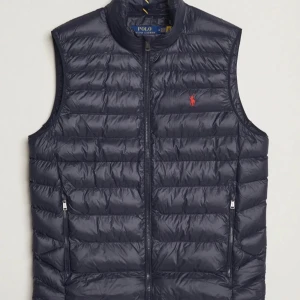 Mörkblå dunväst från Polo Ralph Lauren - Snygg mörkblå dunväst från Polo Ralph Lauren med dragkedja framtill och två fickor med dragkedja. Klassisk quiltad design och liten röd logga på bröstet. Köpt på Zalando, värdebevis och lappar finns.