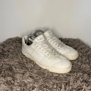 Valentino Flycrews - Säljer ett par klassiska vita Valentino Garavani sneakers i skinn med rund tå och snörning. Skorna har en stilren design med diskret logga på plösen och passar perfekt till en clean och modern look.