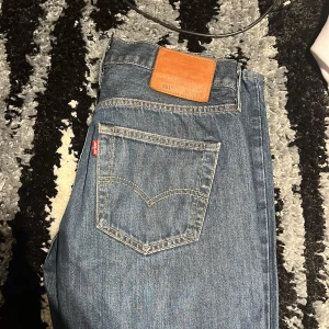 501 jeans  - Klassiska blå Levi's 501 jeans med raka ben och femficksmodell. Ikonisk läderpatch bak i midjan och tydlig röd Levi's-tagg på bakfickan. Gylf med knappar och slitstarka sömmar. Perfekta för en tidlös denimlook. Litet hål nere vid benet, W30/L32