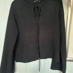 Svart stickad tröja med snörning från Gina Tricot - Svart stickad tröja från Gina Tricot med snygg snörningsdetalj framtill. 