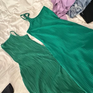 Grön ribbad långklänning med smala axelband - Säljer en snygg grön långklänning med smala axelband och ribbad struktur. Klänningen har en figurnära passform och är perfekt för sommardagar. Enkel och stilren design som passar till många tillfällen.