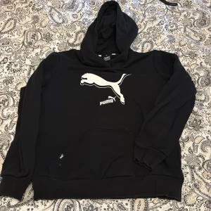 Svart hoodie från Puma - Säljer en svart hoodie från Puma med stor vit logga framtill. Klassisk huva och magficka, perfekt för en avslappnad stil. Mjuk och bekväm, passar till många tillfällen. Den är storlek M i barnstorlekar så tänker att xs borde vara motsvarande 