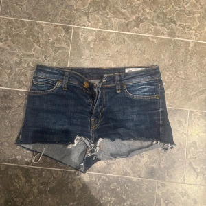 Mörkblå jeansshorts från crocker  - Säljer ett par mörkblå jeansshorts från crocker med råa, fransiga kanter och klassiska fem fickor. Shortsen har låg midja och synliga slitningar för en avslappnad look. Perfekta för sommaren!