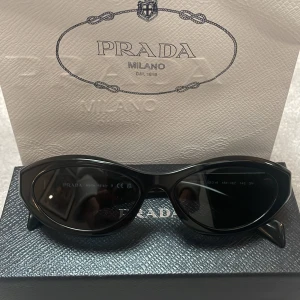 Svarta cat eye solglasögon från Prada - Snygga svarta solglasögon från Prada i cat eye-modell. Glasögonen har en glansig finish och båge med Prada-logga på sidan. Kommer med originalfodral, ask och påse.Perfekt accessoar för en trendig look. Köpta för 1 år sedan i en Prada butik i Rom Italien. Kvitto finns såklart också. Skickar gärna mer bilder på både solglasögonen och andra detaljer om du är intresserad!🙌☺️