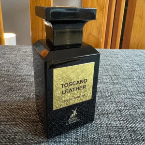 Toscano Leather EDP från Maison Alhambra - Upptäck Toscano Leather, en Eau de Parfum från Maison Alhambra. Denna doft kombinerar läder, animaliska toner, amber och rökiga inslag med träiga och fruktiga noter. Perfekt för både kvinnor och män som söker en varm och kryddig doft med en söt och musky bas. Endast testad. Lådan medföljer ej.