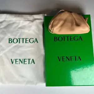 Model: Micro Pouch bag. Kommer med originalförpackning och dustbag. Nypris omkring 30k Säljer en elegant beige handväska från Bottega Veneta. Väskan är tillverkad i mjukt skinn och har en stilren design med rynkade detaljer. Perfekt för att ge en lyxig touch till din outfit. 