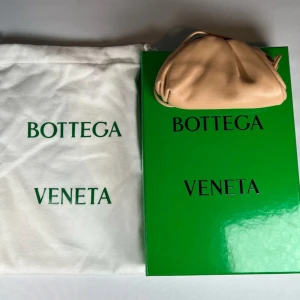 Beige handväska från Bottega Veneta - Model: Micro Pouch bag. Kommer med originalförpackning och dustbag. Nypris omkring 30k Säljer en elegant beige handväska från Bottega Veneta. Väskan är tillverkad i mjukt skinn och har en stilren design med rynkade detaljer. Perfekt för att ge en lyxig touch till din outfit. 