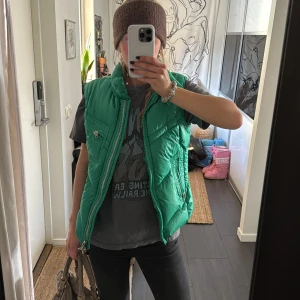 Grön dunväst från J.lindberg - Säljer en snygg grön dunväst från J.Lindberg. Västen har dragkedja och flera praktiska fickor med dragkedjor. Sjukt cool detalj i outfits!❣️