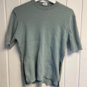 Grön ribbad tröja - Säljer en stilren grön ribbad tröja med korta ärmar. Perfekt för en avslappnad look. Tröjan har en rund halsringning och är tillverkad i ett mjukt material.