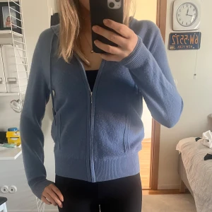 Blå kashmir hoodie från Soft Goat - Säljer en mjuk och stilren blå hoodie från Soft Goat i kashmir. Tröjan har dragkedja framtill och långa ärmar med ribbade muddar. Perfekt för en avslappnad och bekväm stil. Hör av dig vid intresse! 💙