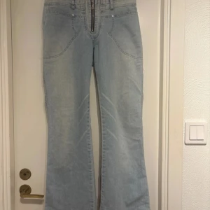Ljusblå bootcut jeans med broderad detalj - Snygga ljusblå bootcut jeans med en unik rosa broderad text på baksidan. Jeansen har en dragkedja framtill. Mått: Midja: 34 cm innerbenslängd: 78 cm. Jag är 165, de är stretchiga. 