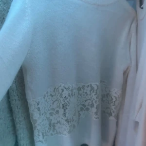 Vit tröja med spetsdetalj från Zara - Säljer en stilren vit tröja från Zara med vacker spetsdetalj runt midjan. Tröjan har långa ärmar och en rund halsringning. Perfekt för en elegant look.