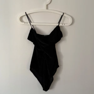 Svart baddräkt med tunna axelband - Snygg svart baddräkt med tunna axelband och elegant design. Perfekt för en stilren look vid poolen eller stranden. Materialet ser ut att vara mjukt och bekvämt.