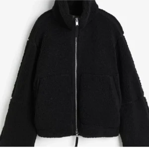 Svart teddyjacka  - Mysig svart teddyjacka med dragkedja framtill och hög krage. Jackan har en avslappnad passform och stora fickor, perfekt för kyliga dagar.