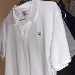 Acne pike - Säljer en stilren vit pikétröja från Acne Studios. Tröjan har en klassisk krage och knappar framtill. Den är dekorerad med Acne Studios ikoniska ansiktslogga på bröstet. Perfekt för en avslappnad men ändå snygg look.