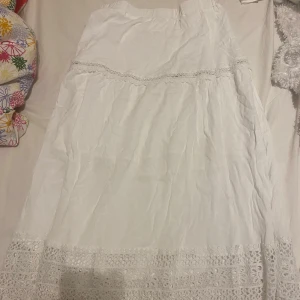 Vit kjol med spetsdetaljer - Säljer en vacker vit kjol med fina spetsdetaljer. Kjolen har en luftig passform och når förbi fötterna Perfekt för varma dagar! 