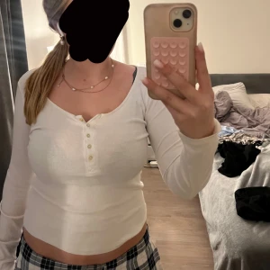 Vit långärmad topp med knappar - Säljer en vit långärmad topp med knappar framtill. Toppen har en v-ringad design och är perfekt för en stilren look. Passar bra till både jeans och kjol.