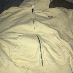 Gul hoodie från Zara - Säljer en gul hoodie från Zara med texten 'BEACH WAVES KEEP IT ON THE WEST COAST' tryckt på bröstet och en bild på baksidan. Hoodien har en dragkedja framtill och en stor ficka. Perfekt för en avslappnad stil.