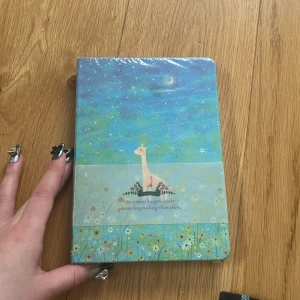 Anteckningsbok med giraffmotiv - Säljer en söt anteckningsbok med ett färgglatt omslag som visar en giraff under en stjärnklar himmel. Omslaget har en text och blommönster längst ner. Perfekt för att skriva ner dina planer och idéer. Innersidor har olika design och färger 