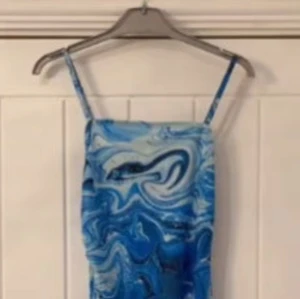 Blå mönstrad klänning - Snygg blå klänning med ett unikt mönster som påminner om virvlande vatten. Klänningen har smala axelband och en figurnära passform. Perfekt för att sticka ut med stil!