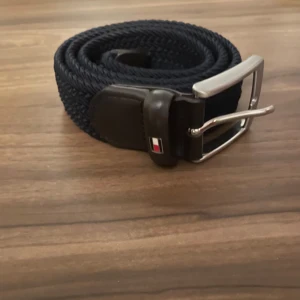 Blått flätat bälte från Tommy Hilfiger - Snyggt blått flätat bälte från Tommy Hilfiger med ett stilrent silverfärgat spänne. Kostar omkring 500 nypris och är i storlek 85❗️Absolut nyskick 10/10 alltså inga som helst slitage märken eller missfärgning. Lite ljusare än på bilderna❗️Kan gå ner lite i pris 