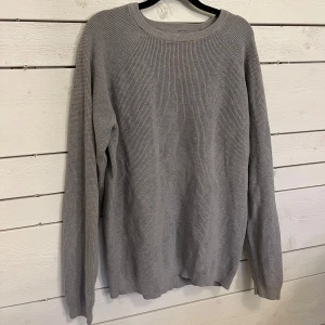 Grå stickad tröja från Dressmann - Säljer en stilren grå stickad tröja från Dressmann. Tröjan har en klassisk design med långa ärmar och rund halsringning. Perfekt för kyligare dagar och enkel att matcha med olika outfits! På höger arm är det en liten mask men det är lätt att fixa😊