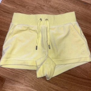 Gula shorts från Juicy Couture - Snygga gula shorts från Juicy Couture i mjukt material. De har en bred resår i midjan med snörning och två fickor fram. Perfekta för en avslappnad stil.