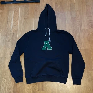 Svart Axel Arigato hoodie - Säljer en svart axel arigato hoodie med ett stort grönt 'A' på bröstet. Kostade 1600 kr. Hoodien har en klassisk design. Perfekt för en avslappnad stil. Passar bra på någon runt 176-180 cm. (Vet inte hur storlekarna fungerar)