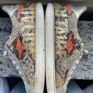 Zadig & Voltaire Sneakers med ormskinnsmönster - Unika Zadig&Voltatie sneakers med ett iögonfallande ormskinnsmönster. Skorna har snörning och en vit sula. Perfekta för dig som vill sticka ut med en djärv stil.