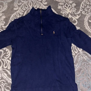 Blå tröja från Ralph Lauren - Säljer en snygg blå tröja från Ralph Lauren med dragkedja och broderad logga på bröstet. Perfekt för en stilren look.