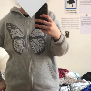 Grå hoodie med fjärilsmotiv - Säljer en grå hoodie med dragkedja och ett stort fjärilsmotiv i svart på framsidan. Den har en bekväm passform och är tillverkad i mjukt material. Köpt på vinted, använd ett fåtal gånger. Köpte den för 80 kronor, säljer för 60 kronor. 