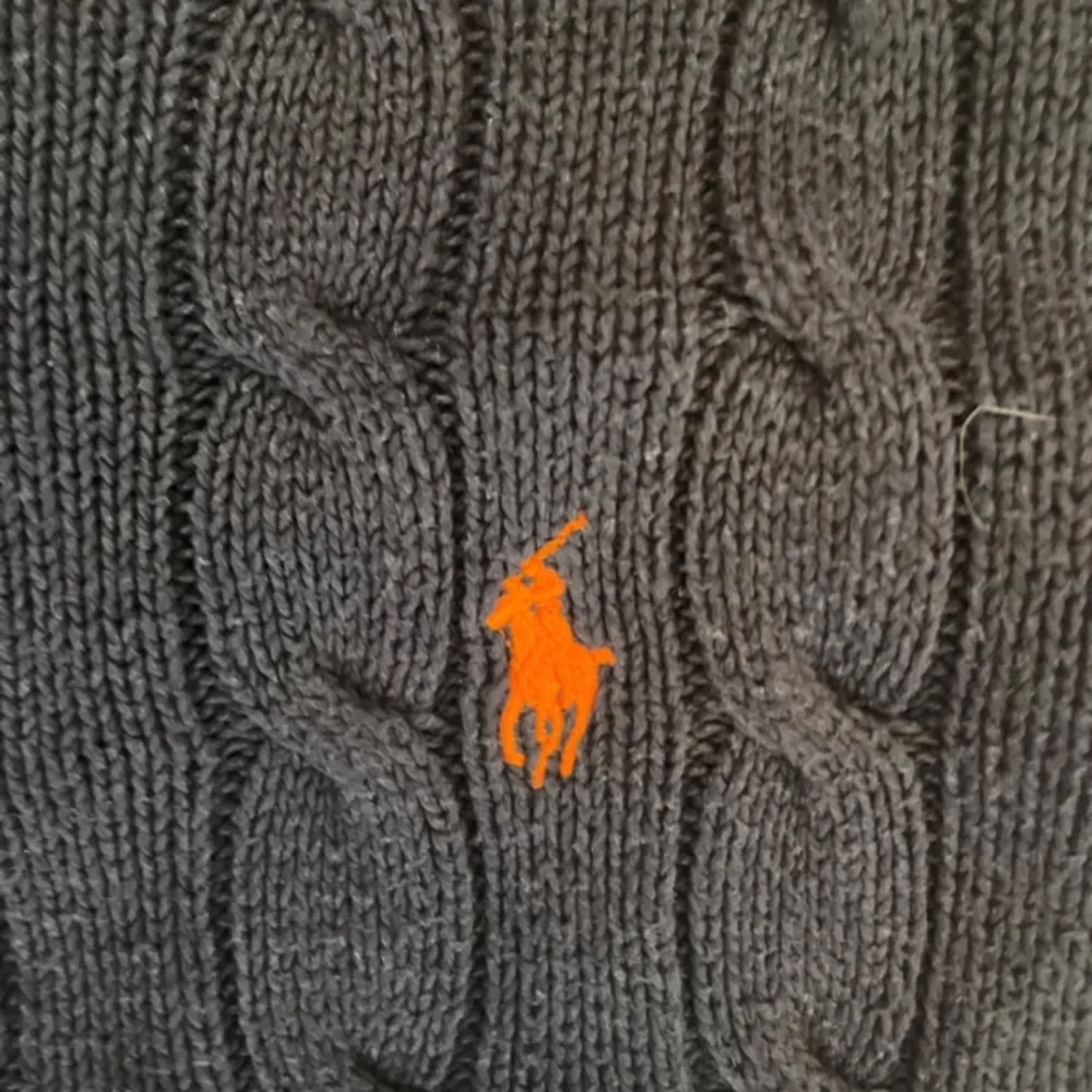 Säljer en snygg mörkblå stickad tröja från Ralph Lauren med det klassiska broderade logotypen i orange på bröstet. Tröjan har ett kabelstickat mönster och långa ärmar. Perfekt för en stilren look!. Neuletakit & Villapaidat.