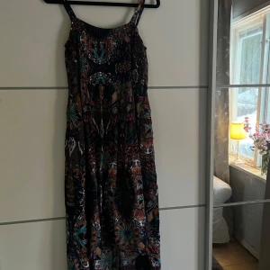Mönstrad klänning från Janina - Säljer en färgglad och mönstrad klänning från Janina. Klänningen har smala axelband och ett livfullt mönster i flera färger som ger en bohemisk känsla. Perfekt för en avslappnad och stilfull look.