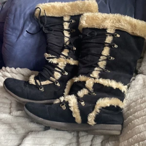 Svarta vinterstövlar med fuskpäls - Snygga svarta stövlar med beige fuskpälsdetaljer och snörning. Perfekta för kalla vinterdagar med en robust sula för bra grepp. De har en mysig och varm insida som håller fötterna varma.