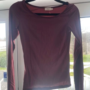 Vinröd långärmad topp från Nelly - Säljer en stilren vinröd långärmad topp från Nelly. Perfekt för både vardag och festliga tillfällen. Toppen har en enkel design med rund halsringning.