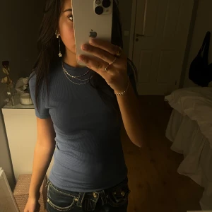 Blå ribbad t-shirt - Säljer en snygg blå lite ribbade t-shirt med korta ärmar. Perfekt för en avslappnad stil och lätt att matcha med jeans eller kjol. Längst ner på baksidan av tröjan är det en söm som gått upp, men inget som märks av!💕