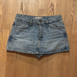 Blå jeansshorts/ kjol  från Zara - Säljer ett par klassiska blå jeansshorts från Zara. De har en hög midja och femficksdesign med knapp och dragkedja framtill. Perfekta för sommardagar! 💙det har en fin look med kjol på framsidan och shorts på baksidan och knappt använda med fint skick,jag skulle säga att dem passar 34 också 💗💗