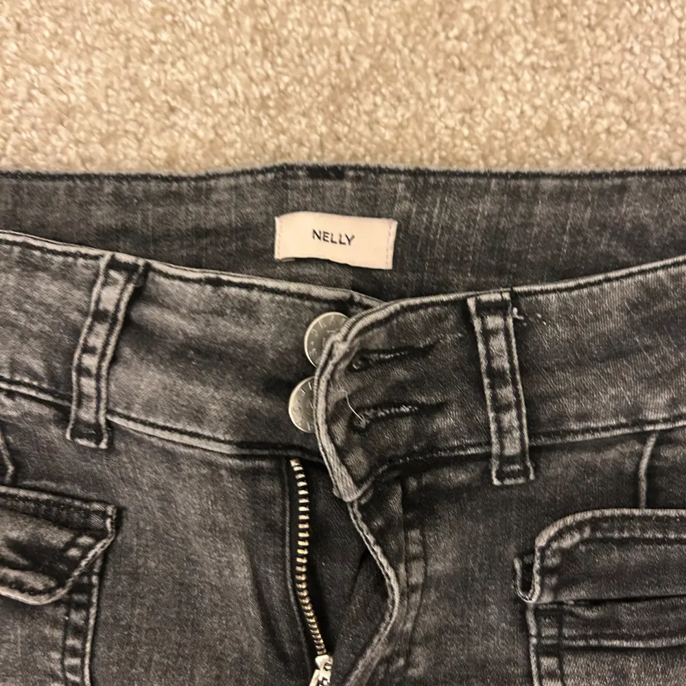 Snygga grå bootcut jeans från Nelly med låg midja. De har framträdande sömmar och fickor både fram och bak. Perfekta för en trendig look. Lite slitningar nere vid fötterna men inget man tänker på. Stretchiga så väldigt sköna!. Farkut & Housut.