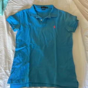 Blå pikétröja från Ralph Lauren - Säljer en snygg blå pikétröja från Ralph Lauren med klassisk krage och korta ärmar. Tröjan har en rosa logotyp på bröstet och är perfekt för en stilren look. Passar både till jeans och chinos. Skriv vid frågor och funderingar 🌟