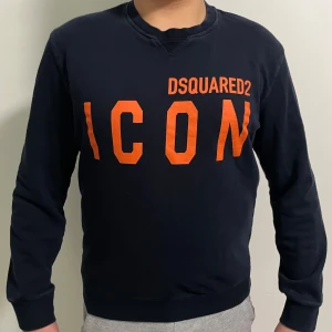 Svart tröja från Dsquared2 - Snygg marinblå tröja från Dsquared2 med orange text 'ICON' på framsidan. Tröjan har långa ärmar och en klassisk rund halsringning. Storlek L men är i passform för M. Tröjan är Äkta men inget kvitto medgår i köpet därför kan pris diskuteras. 