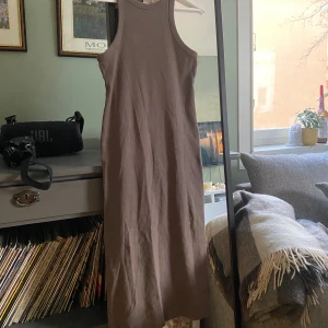 Beige ärmlös klänning - Säljer en stilren beige klänning med ärmlös design. Klänningen har en tight passform och är perfekt för en minimalistisk look. Den är gjord i ett mjukt material som känns skönt mot huden.