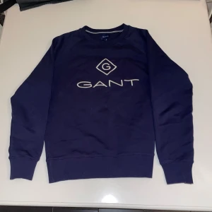 Mörkblå tröja från GANT - Säljer en riktigt snygg mörkblå tröja från GANT, med deras ikoniska logga på bröstet. Tröjan har en bra passform och är riktigt snygg! Tröjan har en rund halsringning med ribbade kanter. Tröjan är perfekt för dig som vill ha en riktigt fet tröja som sitter extremt bra, och till ett bra pris! Skick 9/10, Pris: 139, om du har några funderingar kring tröjan, eller tröjans pris så kan du höra av dig i pm.