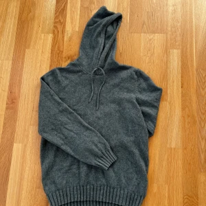 Tunn hoodie - Säljer en stilren grå hoodie från Dressmann. Tröjan är stickad med ribbade muddar och har en justerbar huva med snören. Perfekt för kyliga dagar.