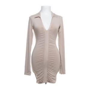 Beige Mini Dress, Ohpolly - Snygg beige klänning med lång ärm och v-ringning. Klänningen har en åtsittande passform med rynkade detaljer med en smickrande passform. Helt ny med prislapp! 