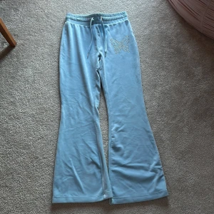 Ljusblått mjukis sätt med fjärilsdetalj - Säljer ett ljusblått mjukis sätt med en snygga fjärilsdetaljer i på ena benet och på bröstet. Byxorna har en bekväm resårmidja med snörning och vida ben. Perfekta för en avslappnad stil.